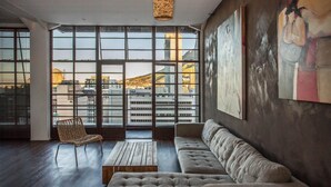 Une pièce spacieuse avec de grandes fenêtres, un luminaire en fibres tressées, un canapé, un fauteuil et une table basse.