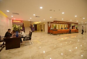 A hotel lobby with a reception desk, seating area, and a staircase leading to other floors.