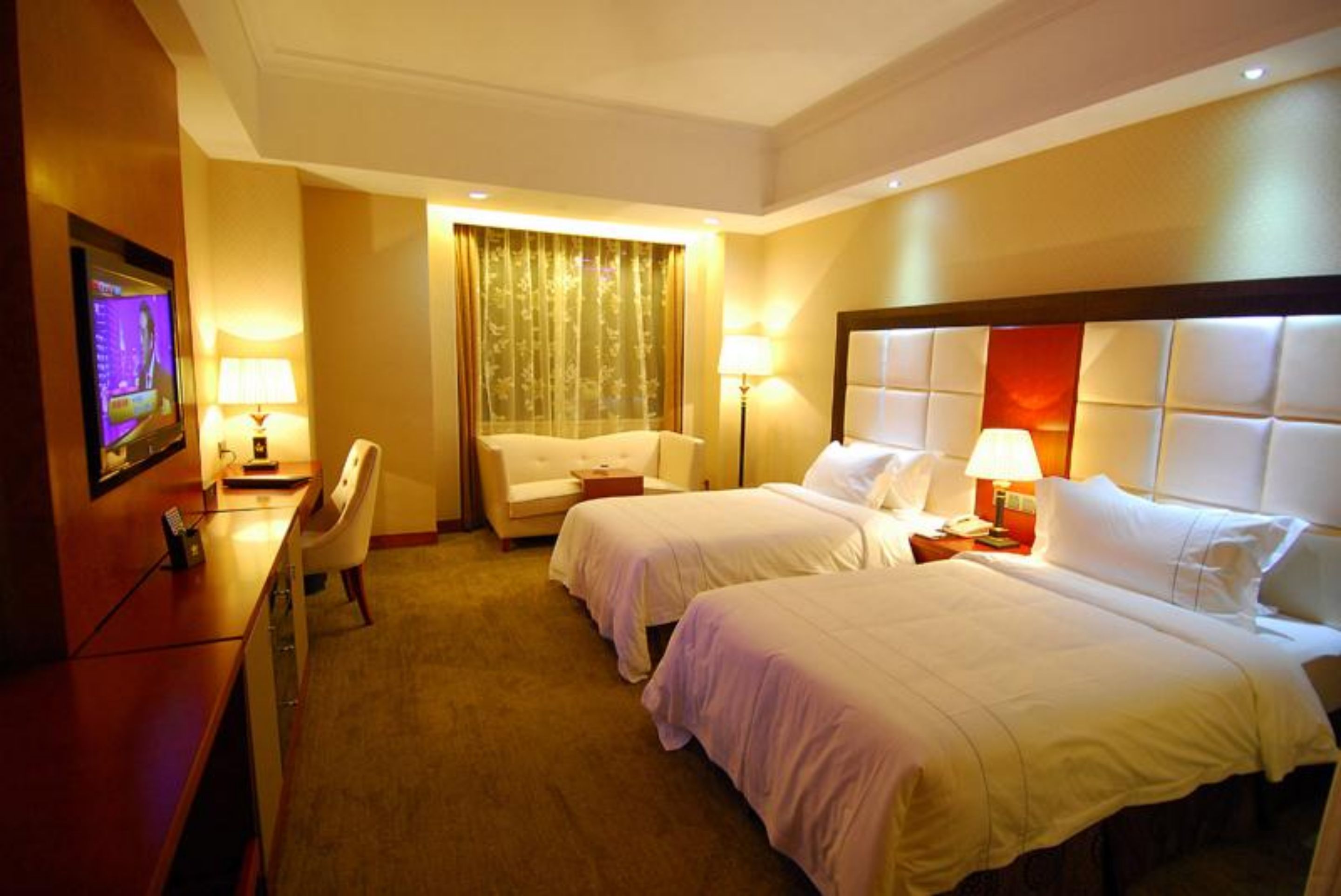 A hotel room with two beds, a desk, a chair, and a TV.