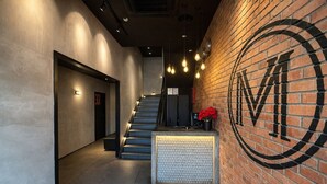 A modern hotel lobby with a staircase, a reception desk, and a large logo on the wall. - Monaco Boutique Hotel Kampung Air (Kota Kinabalu)