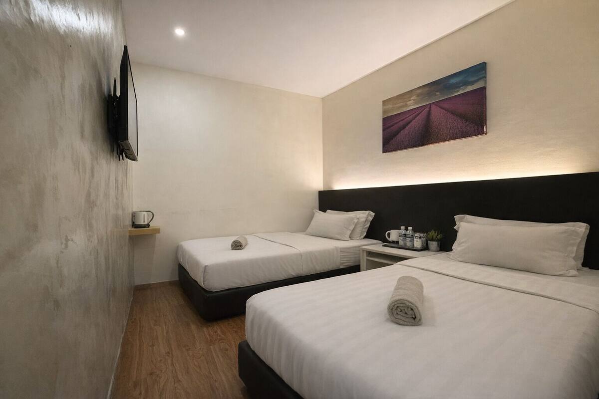 Ein Hotelzimmer mit zwei Betten, einem kleinen Tisch mit Pflanze, einem Bild an der Wand und einem an der Wand befestigten Fernseher.