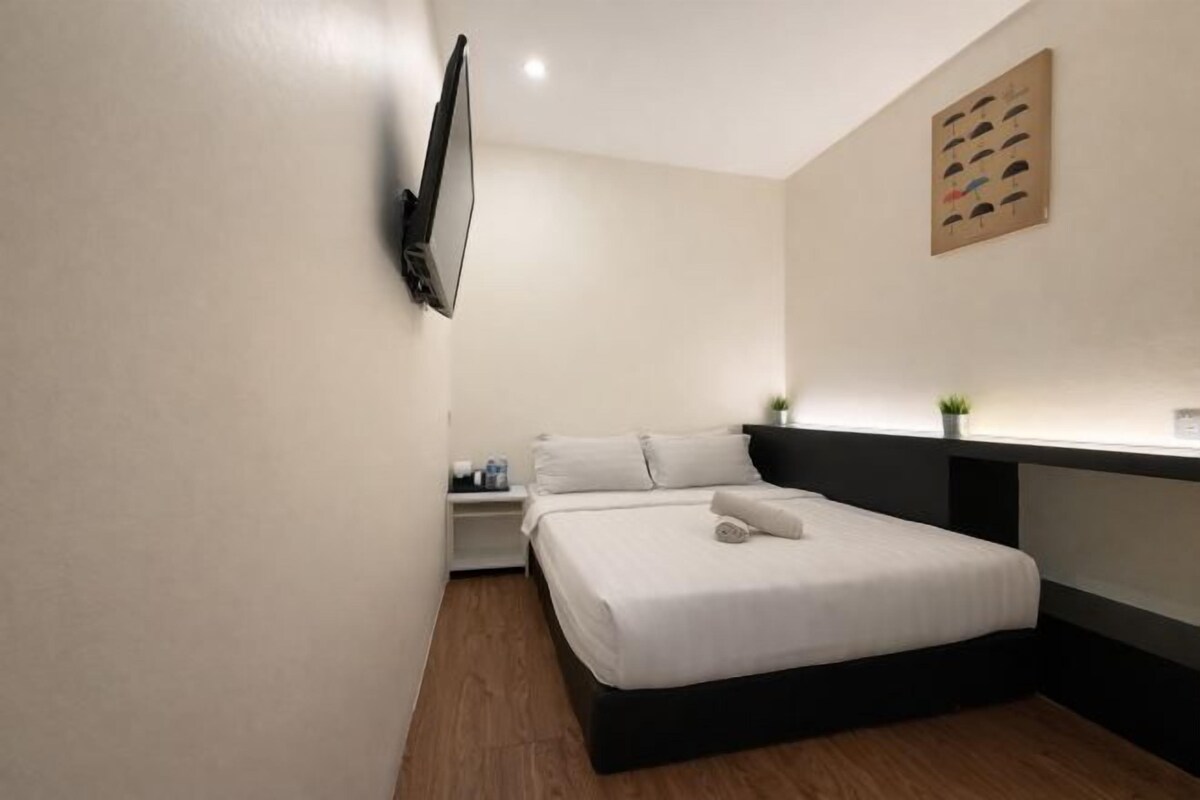 Een moderne hotelkamer met een bed, een flatscreen televisie, een klein nachtkastje en een kunstwerk aan de muur.
