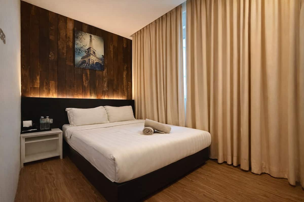 Ein Hotelzimmer mit Bett, Nachttisch, einem Bild des Eiffelturms und beigen Vorhängen.