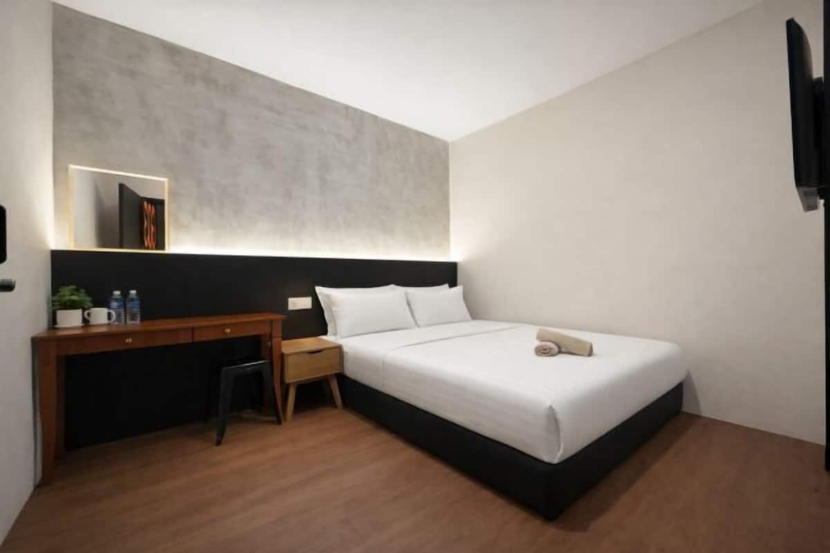 Ein modernes Hotelzimmer mit Bett, Nachttisch, Schreibtisch und einem kleinen Hocker.