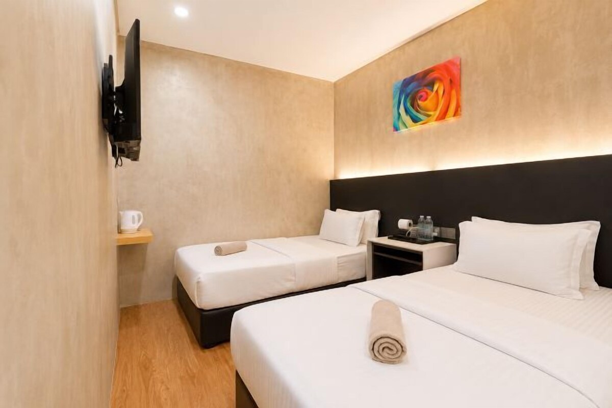 A hotel room with two beds, a flat-screen TV mounted on the wall, a small table with a coffee maker, and a colorful abstract painting above the headboard.