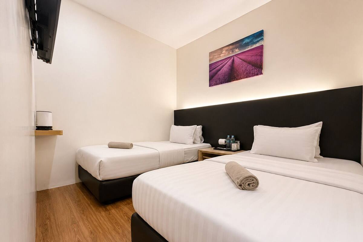 Ein Hotelzimmer mit zwei Betten, Holzboden, einem Bild an der Wand und einem kleinen Tisch mit einer Lampe.