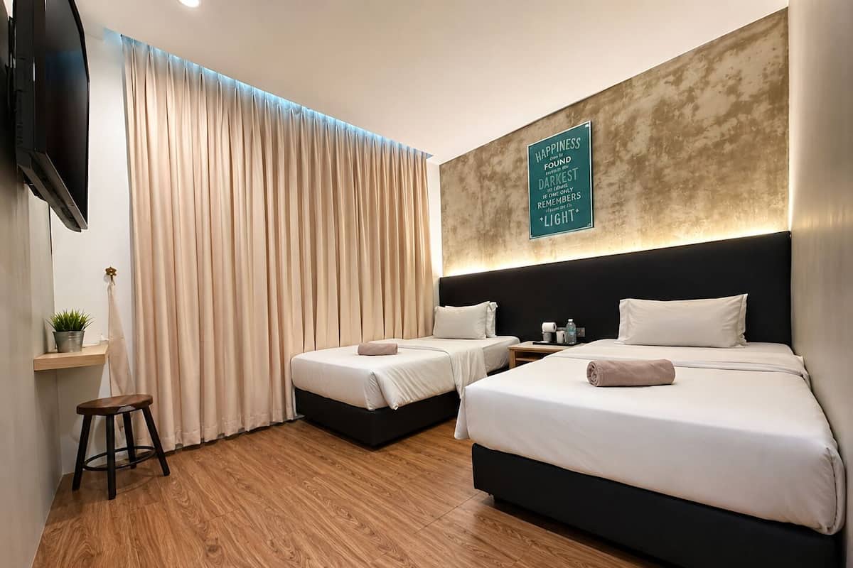 Ein Hotelzimmer mit zwei Betten, einem Fernseher, einer Ablage mit einer Pflanze und einer Wand mit einem motivierenden Zitat.