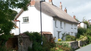 Un bâtiment blanc avec un toit de chaume, un mur de pierre et une rue étroite.