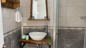 Un baño con un lavamanos grande de color blanco, un estante de madera sobre el lavabo y un espejo.