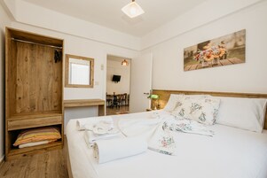 Un dormitorio ordenado con un armario de madera, una cama con ropa de cama floral, un cuadro en la pared y una mesita de noche con una lámpara.