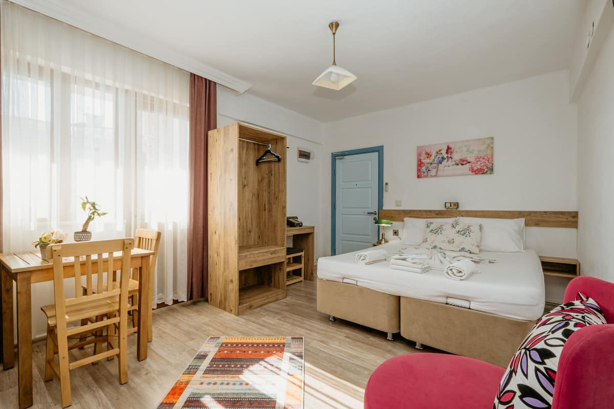 A hotel room with a bed, a desk, a chair, a wardrobe, and a painting on the wall.