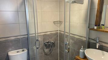Un baño moderno con ducha envuelta en vidrio, inodoro blanco y tocador de madera con un lavamanos grande.
