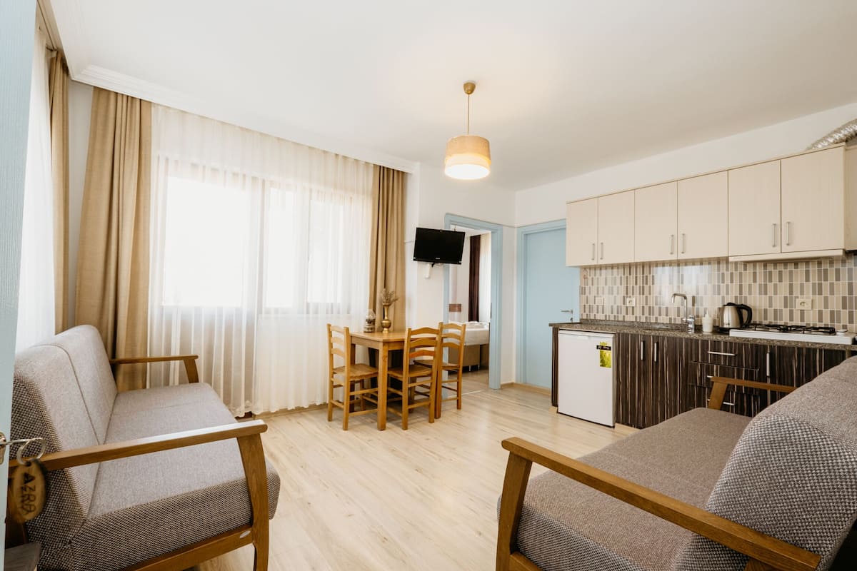 A modern living room with a sofa, a dining table with chairs, and a kitchen area with cabinets and a TV.