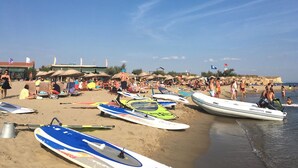 A beach with multiple surfboards lined up, umbrellas, and people enjoying the beach. - Azra Apart & Otel (Gökçeada)
