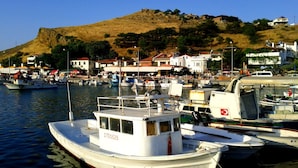 A marina with various boats docked, a hill with buildings in the background, and a clear sky. - Azra Apart & Otel (Gökçeada)