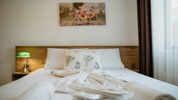 A neatly made bed with a floral pillow, a green lamp on a wooden nightstand, and a painting of flowers on the wall.