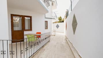 Un pasillo estrecho con una puerta de madera, una mesa con sillas y un pequeño jardín.