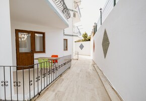 Un pasillo estrecho con una puerta de madera, una mesa con sillas y un pequeño jardín.
