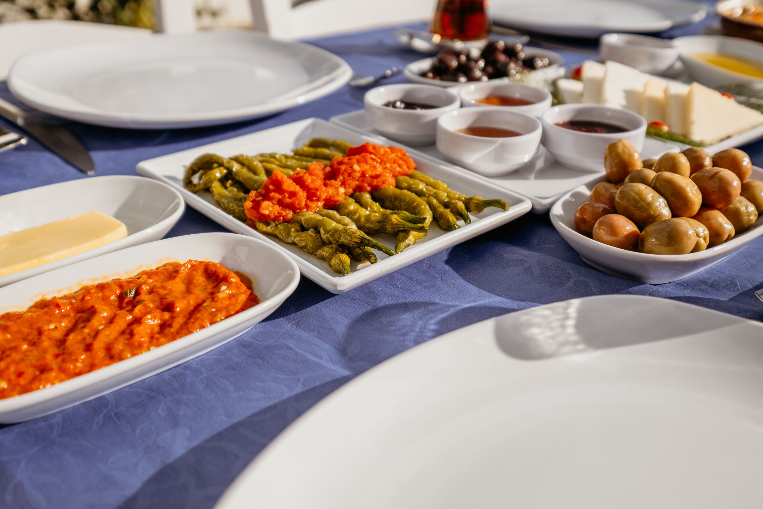 Une table dressée avec différents plats, notamment une assiette de légumes verts, un bol d’olives et un plat de sauce rouge.