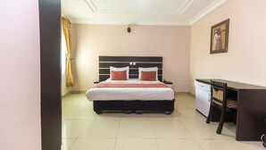 A bedroom with a bed, desk, and chair, a small cabinet, and a painting on the wall. - Royal Terrace Hotel & Towers (Lagos)