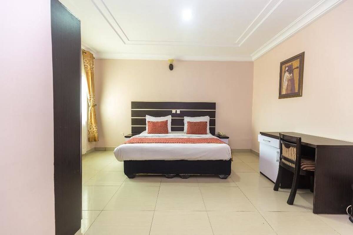 A bedroom with a bed, desk, and chair, a small cabinet, and a painting on the wall.