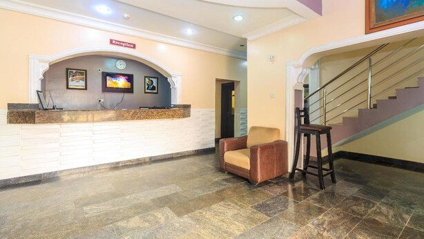 A reception area with a reception desk, a clock, a TV, and a staircase. - Royal Terrace Hotel & Towers (Lagos)