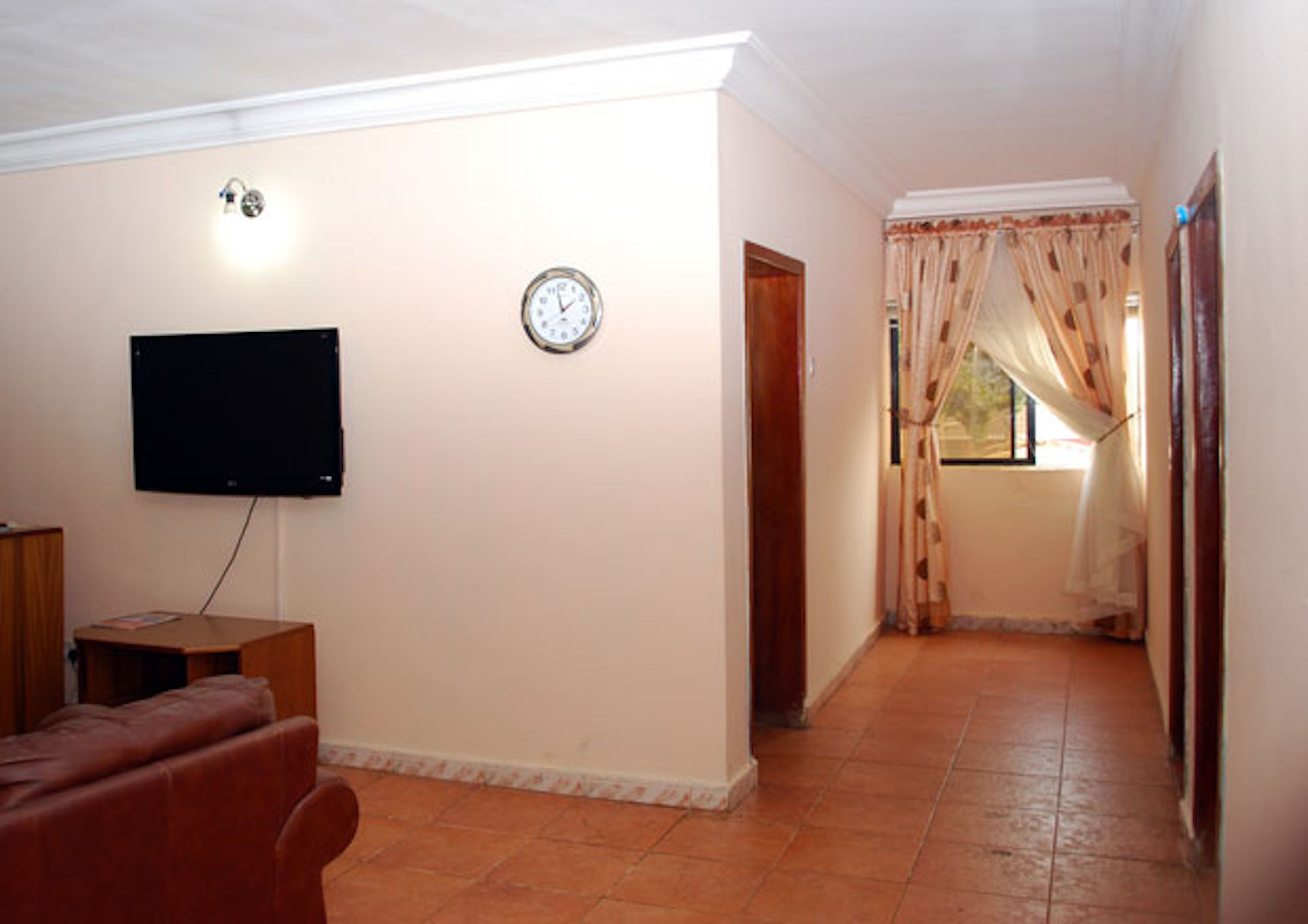 A living room with a flat-screen TV, a clock, a sofa, and a window with curtains.