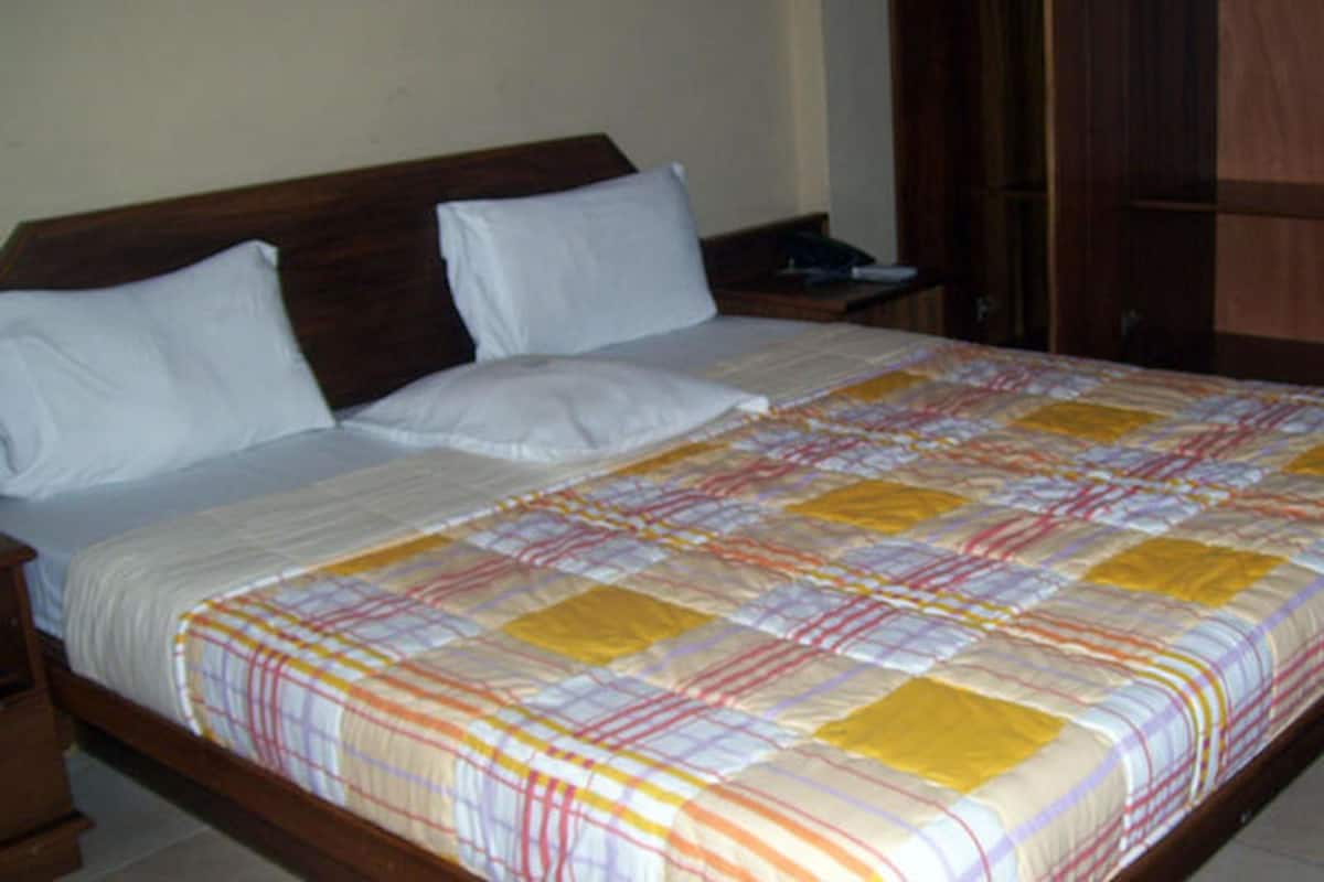 Een standaard hotelkamer met een houten bedframe, wit beddengoed en een kleurrijk sprei.