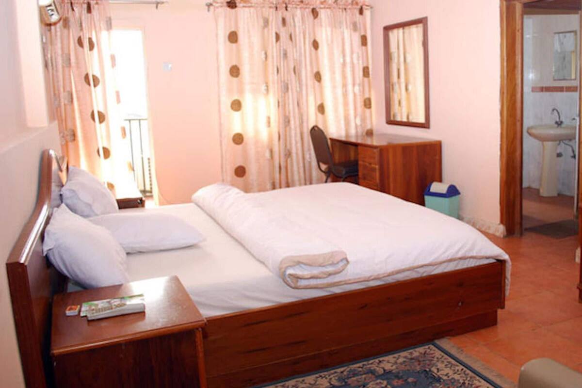 Een slaapkamer met een houten bed, een bureau, een stoel, een spiegel en een badkamer zichtbaar door een geopende deur.
