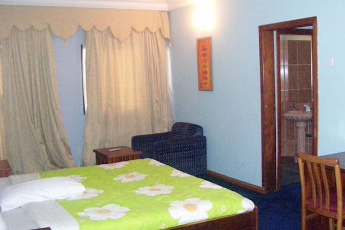 Een slaapkamer met een bed, een stoel, een klein tafeltje en een badkamer zichtbaar door een geopende deur.