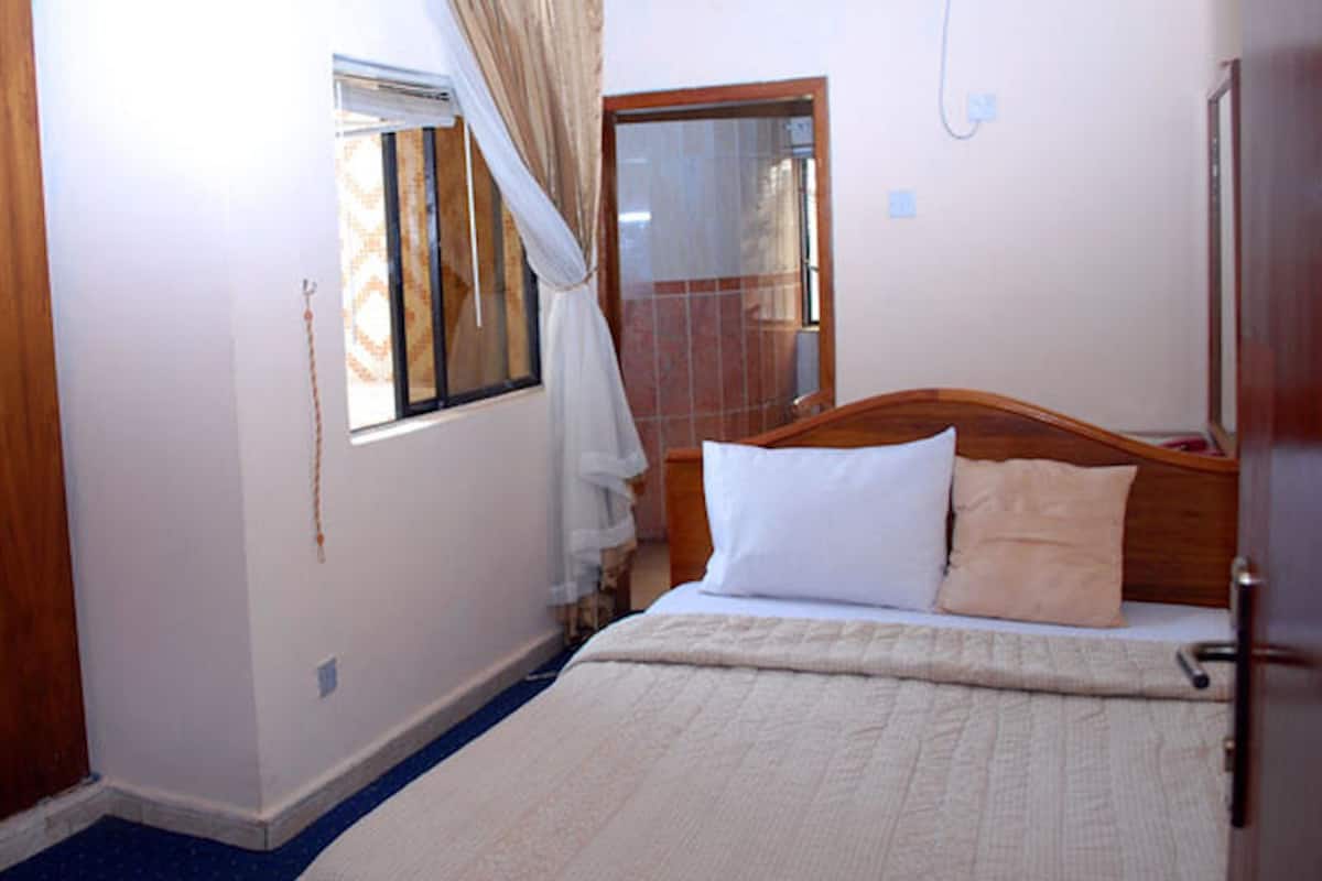 Een slaapkamer met een bed, een raam met gordijnen, een houten hoofdeinde en een blauw vloerkleed.