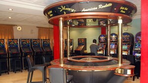 Eine Spielhalle mit zahlreichen Spielautomaten, einer zentralen runden Theke und einigen Barhocker.