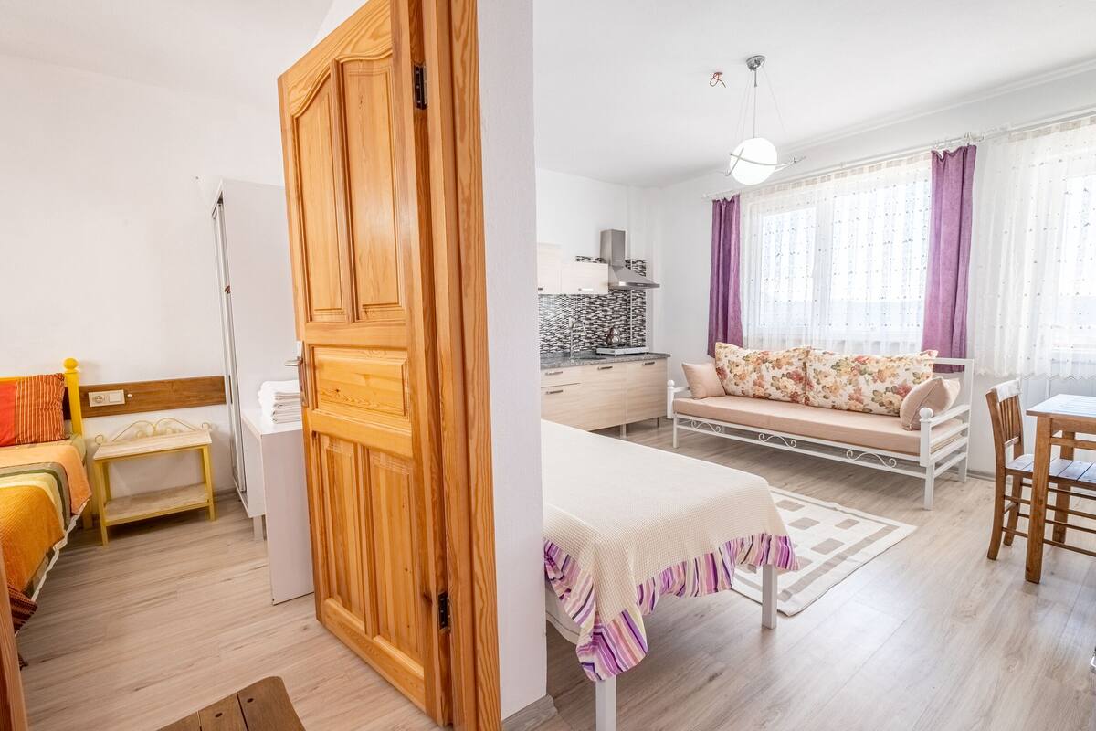 Ein Zimmer mit einem Bett, einem Holzschrank, einem kleinen Tisch, einer Couch und einer Essecke mit Stühlen.