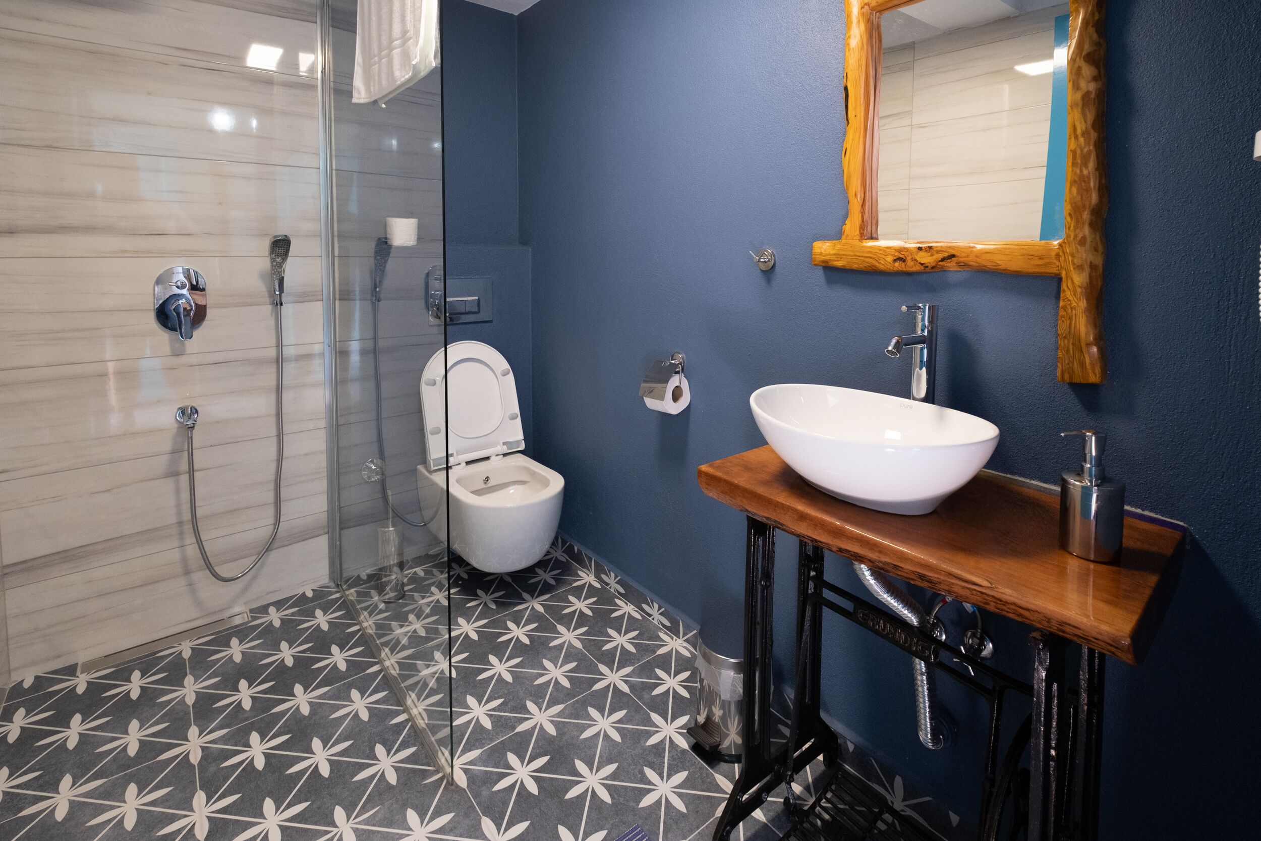 A bathroom with a glass shower enclosure, a toilet, a sink with a wooden countertop, and a mirror with a wooden frame.