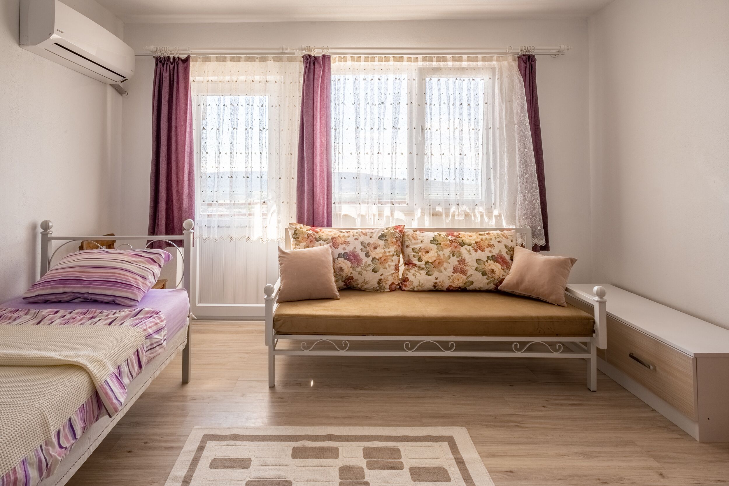 A bedroom with a bed, a sofa, a bedside table, and a window with curtains.