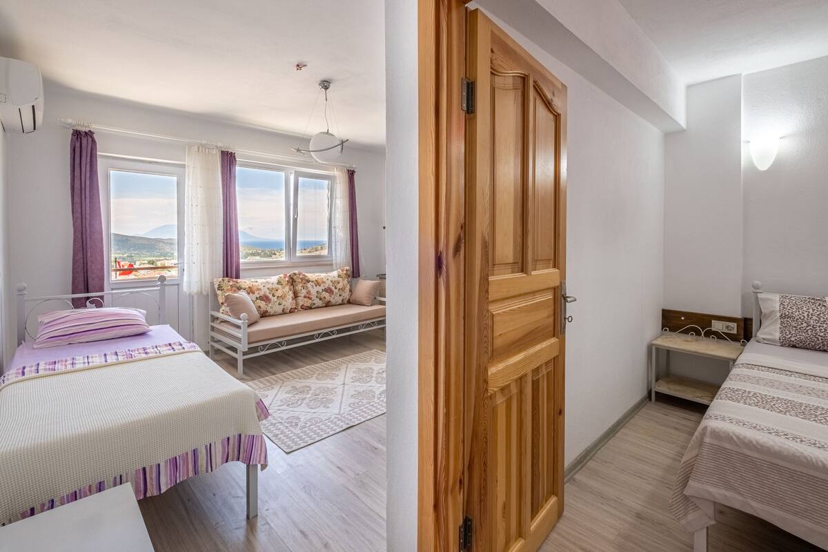 Ein Schlafzimmer mit Bett, Fenster mit Aussicht, Holztür und einem kleinen Nachttisch.