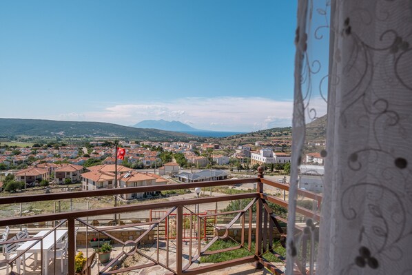 Un balcón con vistas a una zona residencial, una bandera y un paisaje montañoso en la distancia.