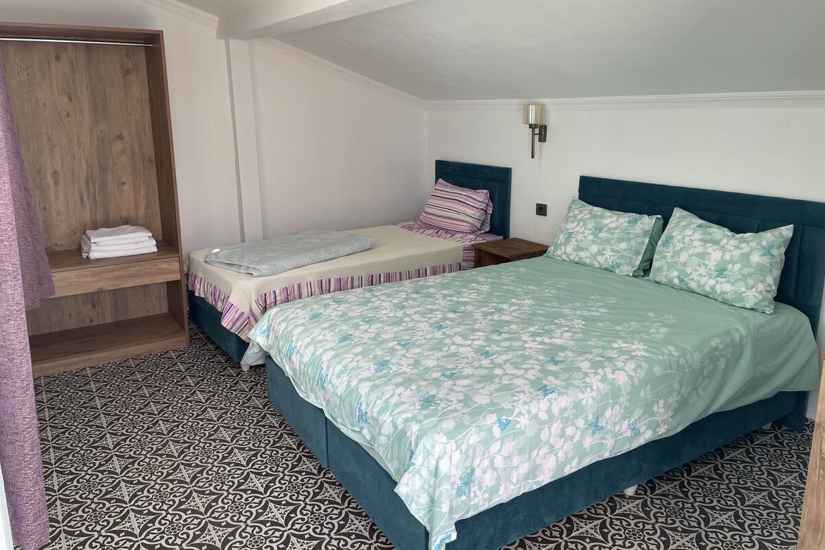 Ein Schlafzimmer mit einem großen Bett, einem kleineren Bett, einem Holzschrank und einem fußbodenbündigen Musterparkett.