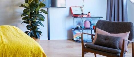 Ein modernes Schlafzimmer mit Bett, Sessel, Pflanze, Fernseher und Schreibtisch mit Laptop.