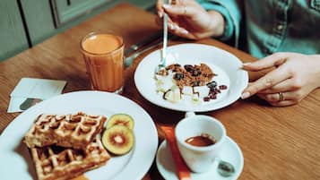 Uma mesa de jantar com waffles, kiwi fatiado, um copo de suco de laranja e um prato com cereais e passas.