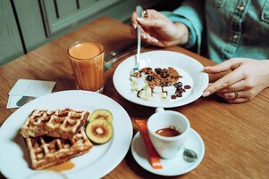 Uma mesa de jantar com waffles, kiwi fatiado, um copo de suco de laranja e um prato com cereais e passas.
