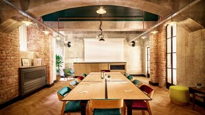 A conference room with a long table, chairs, a projector screen, and a brick wall. - Max Brown Hotel 7th District, part of Sircle Collection (Vienna)
