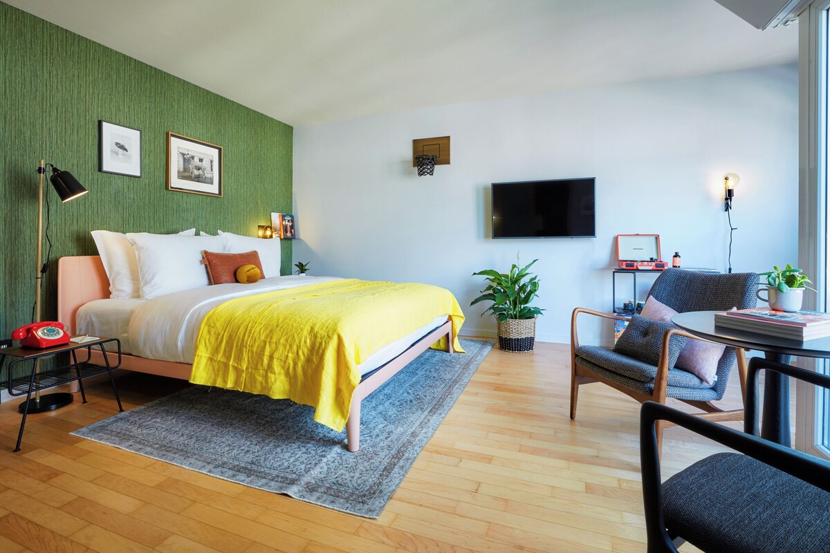 A modern bedroom with a bed, bedside table, lamp, and a small table with a plant.
