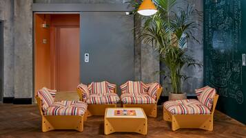 Um lobby com sofás listrados, uma mesa de centro, uma planta em vaso e uma parede de lousa com nomes de quartos.