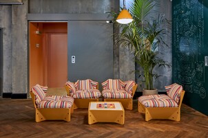 Um lobby com sofás listrados, uma mesa de centro, uma planta em vaso e uma parede de lousa com nomes de quartos.