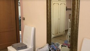 Une salle de bain avec des toilettes blanches, une chaise, un miroir et une armoire.