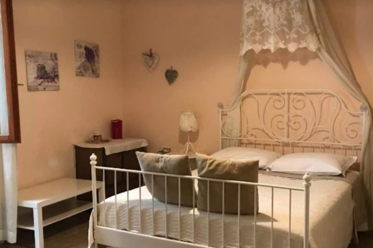 Un dormitorio con cama, mesita de noche, lámpara y una pequeña estantería con adornos.