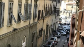 Une rue étroite, bordée de voitures garées et de bâtiments aux fenêtres fermées par des volets.
