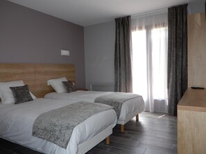 A hotel room with two beds, a wooden headboard, grey curtains, and a wooden desk. - Hôtel restaurant Marinet (Valserhône)