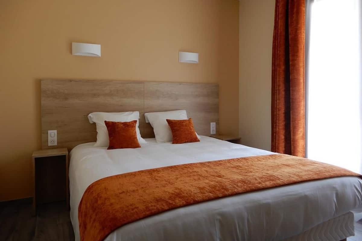 A hotel room with a large bed, two bedside tables, a wooden headboard, and two wall-mounted light fixtures.